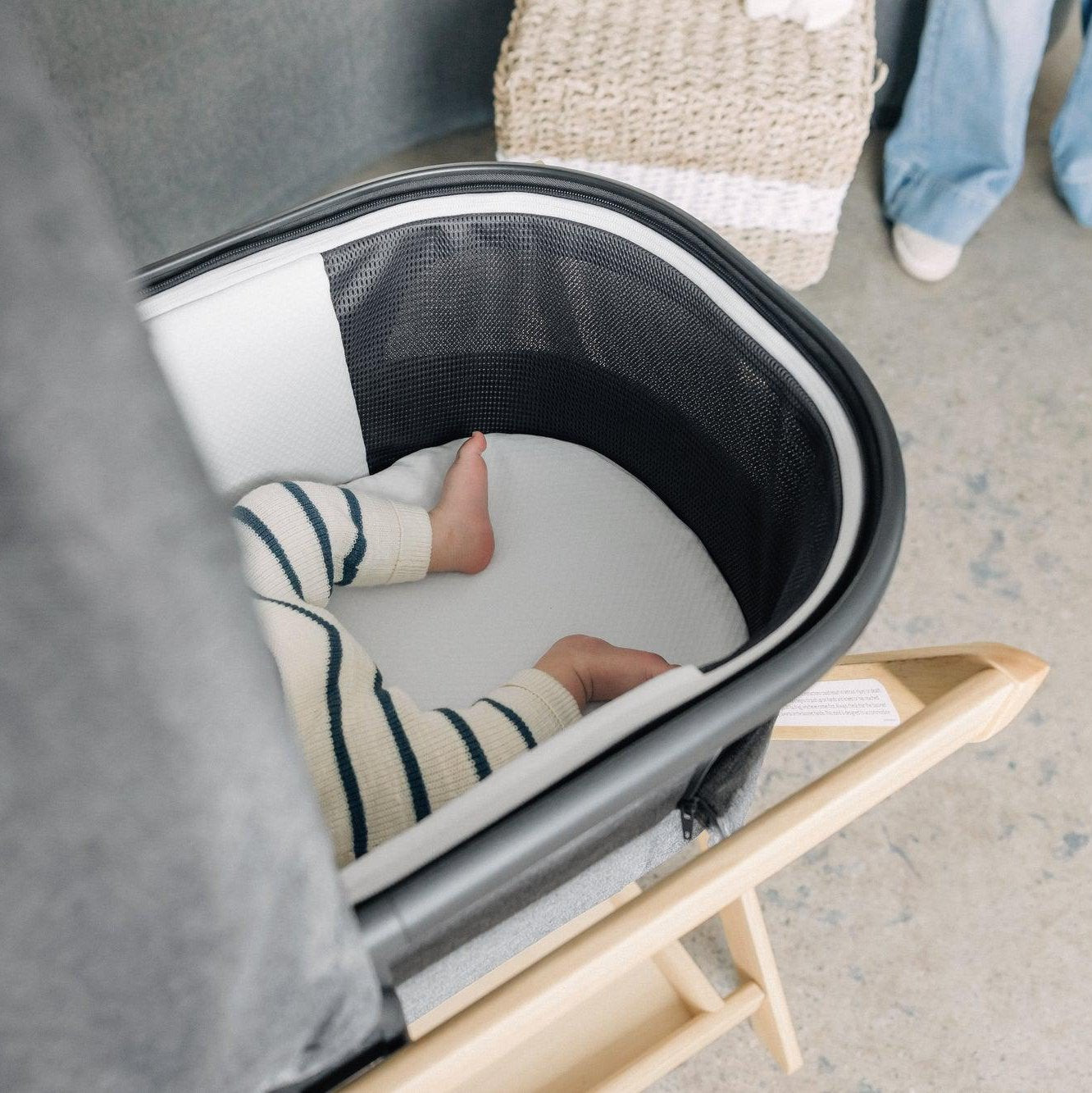 Baby resting inside a bassinet on a natural wood stand