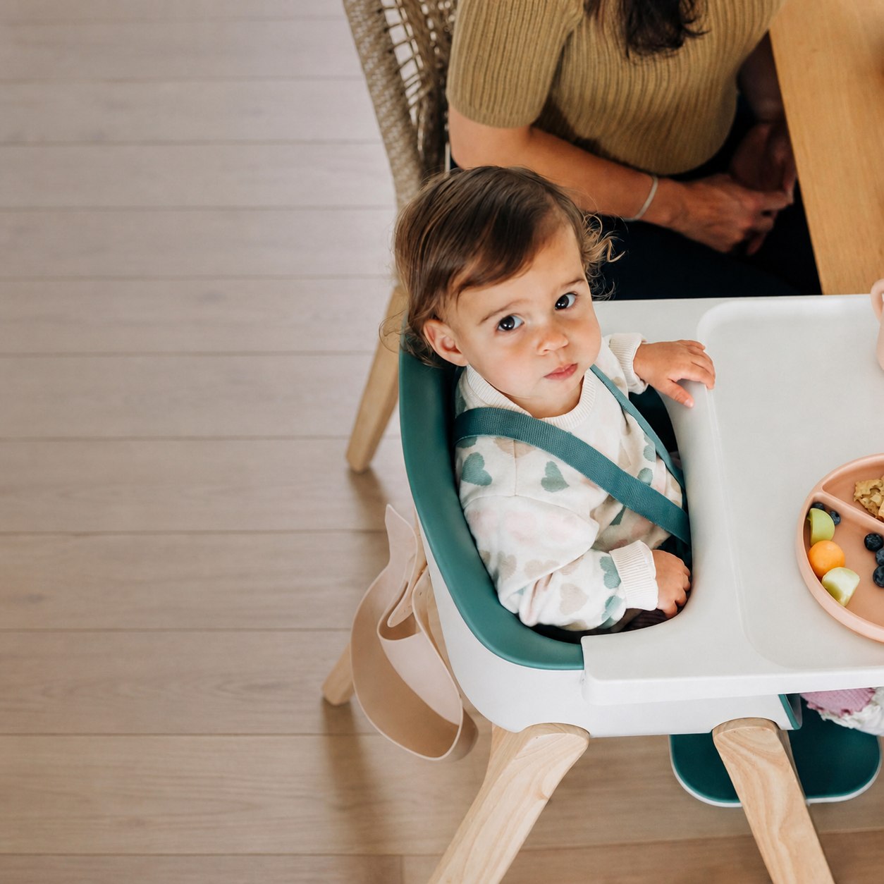 A child seated in a high chair with a caregiver nearby