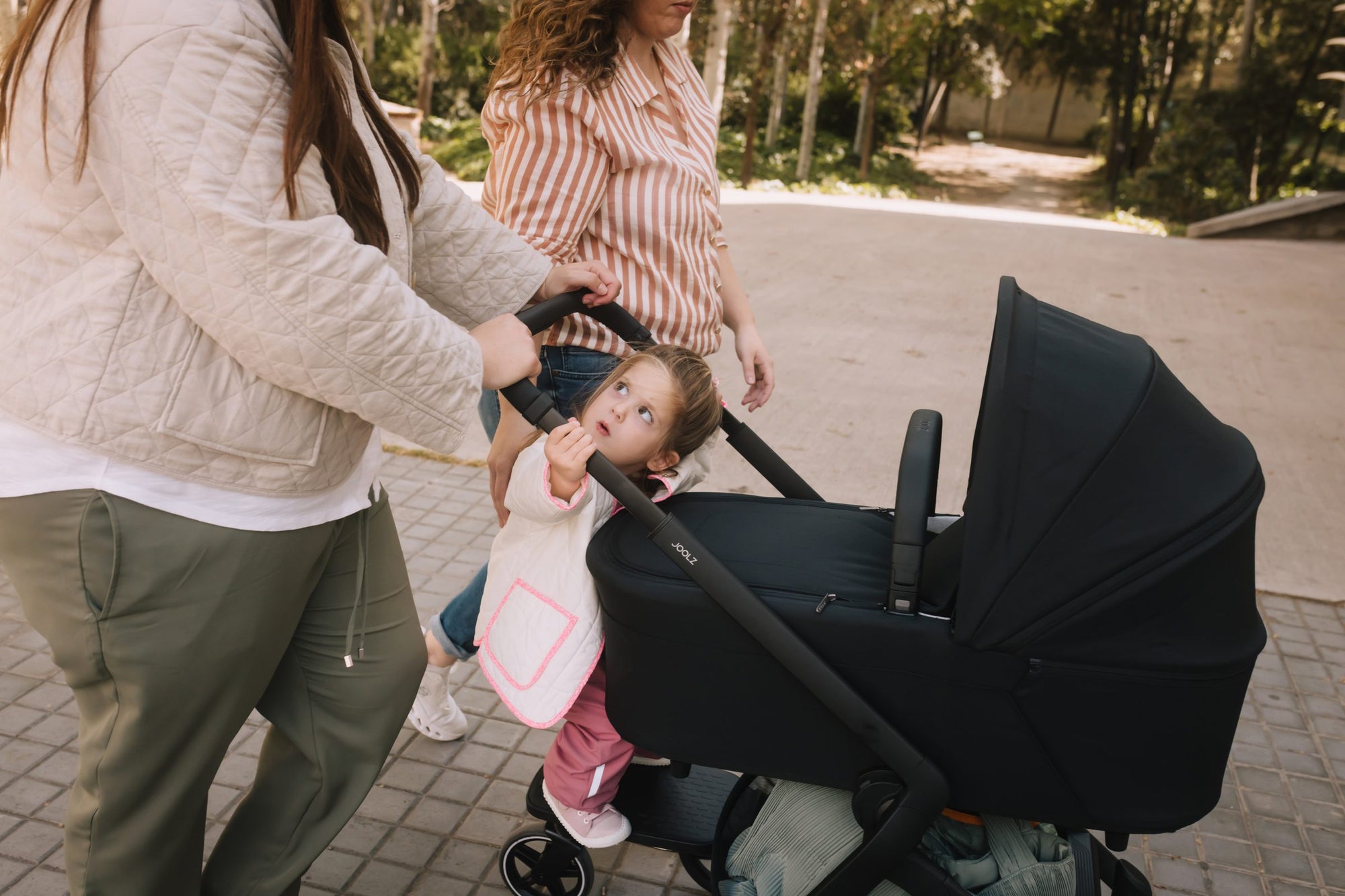 Parent and toddler beside a Joolz Aer bassinet stroller on a quiet street